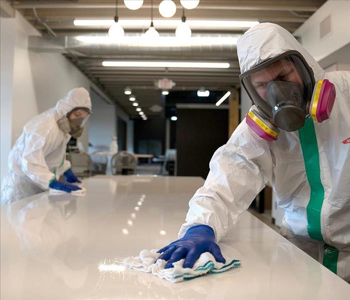 White office table being cleaned by 2 workers in white suits.