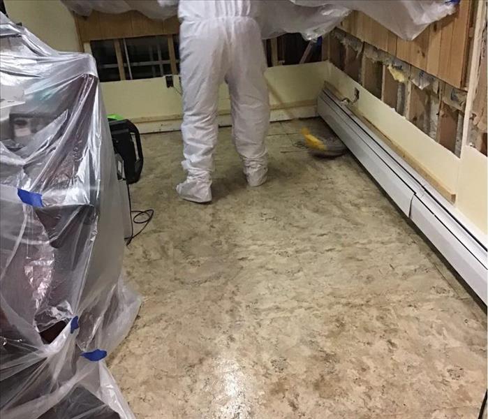 Dirty tile floor with a person in a white suit mopping in the corner of the room.