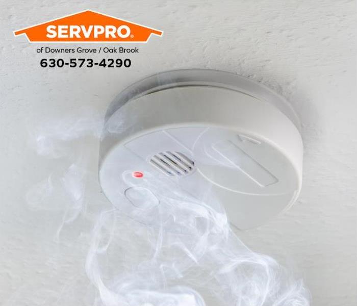 White smoke alarm with smoke on a white ceiling.